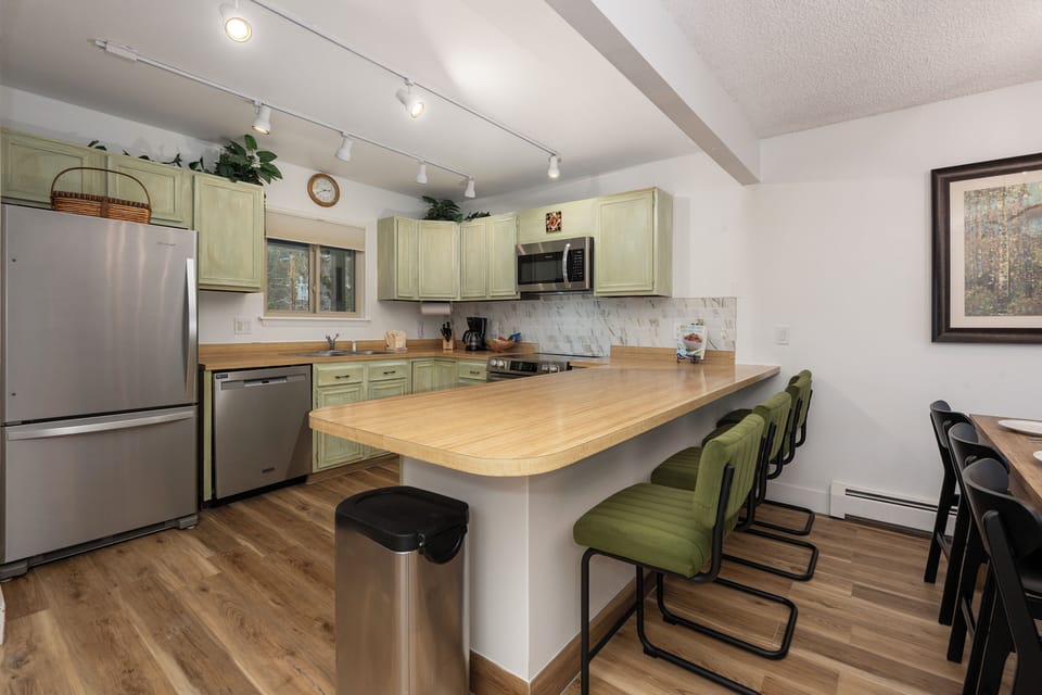 Your fully equipped kitchen features sage-green cabinets, butcher block counters, and a breakfast bar perfect for morning coffee or casual meals together.