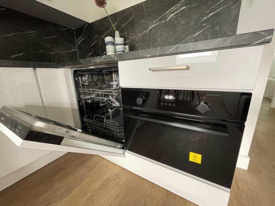 Een moderne keukenkhoek met strakke zwarte apparatuur, waaronder een vaatwasser en oven, tegen elegante marmeren werkbladen.