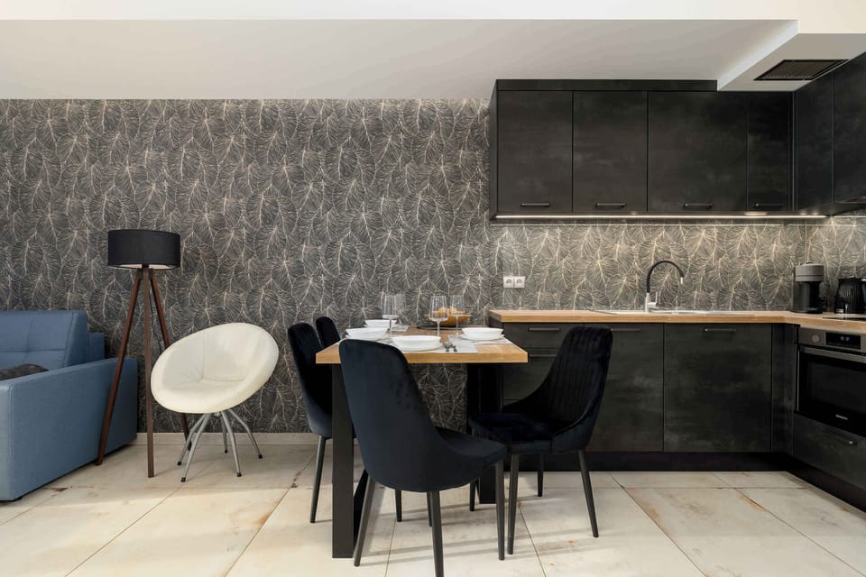 A dining area paired with a sleek kitchen, featuring contemporary chairs, dark cabinetry, and a standing lamp.