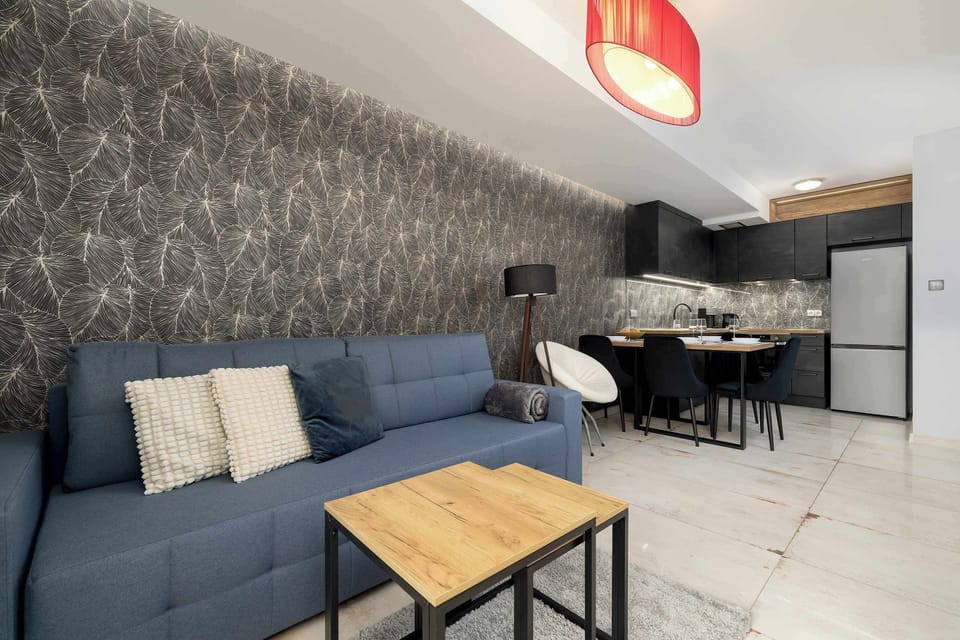 A stylish living and dining zone highlighted by a bold patterned wall, blue sofa, and pendant lighting.
