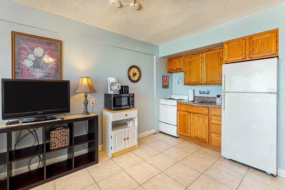 Fully equipped kitchen with classic cabinetry and cozy living area, perfect for a comfortable beach stay. Enjoy easy meal prep, relaxation, and quick access to the beach for sun-soaked days and ocean breezes.