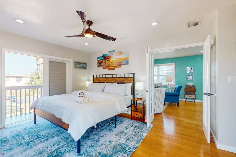 This spacious primary bedroom features a plush bed, beach-inspired décor, ceiling fan, and easy access to the living area and balcony—creating a relaxing and connected retreat for your ideal beach stay.