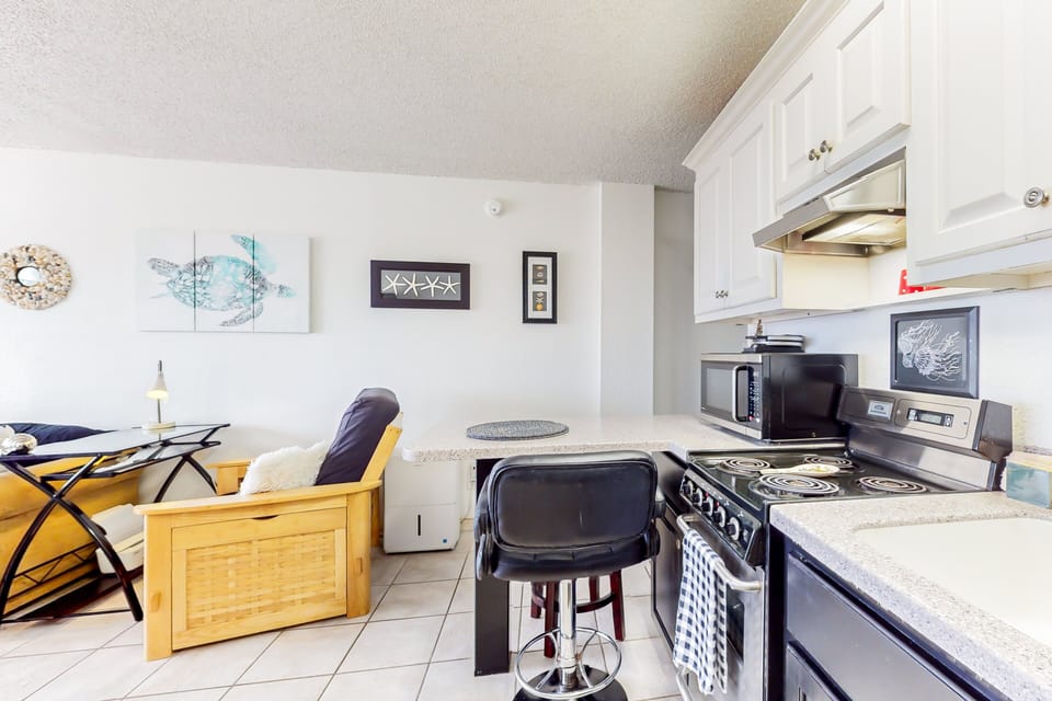 Bright open kitchen and living space with breakfast bar, full appliances, and coastal décor. Ideal for casual meals and relaxing after the beach, offering comfort and convenience during your beach stay.