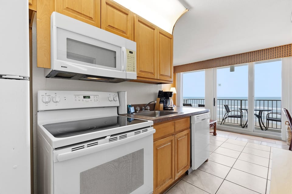 Prepare meals in this fully equipped oceanfront condo kitchen with appliances, coffee maker, and easy access to a private balcony overlooking the beach. Enjoy the comfort and convenience of a relaxing beach stay with beautiful ocean views.