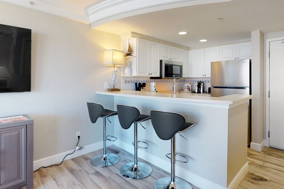Modern beach-stay kitchen with sleek bar seating, stainless appliances, and bright coastal décor—perfect for easy meals before heading out to enjoy the ocean.