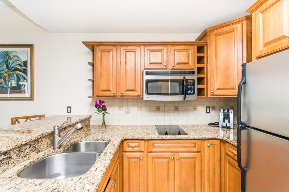 Cook with ease in this bright beach-stay kitchen featuring granite countertops, stainless appliances, and warm wood cabinetry—perfect for preparing meals after a day by the shore.