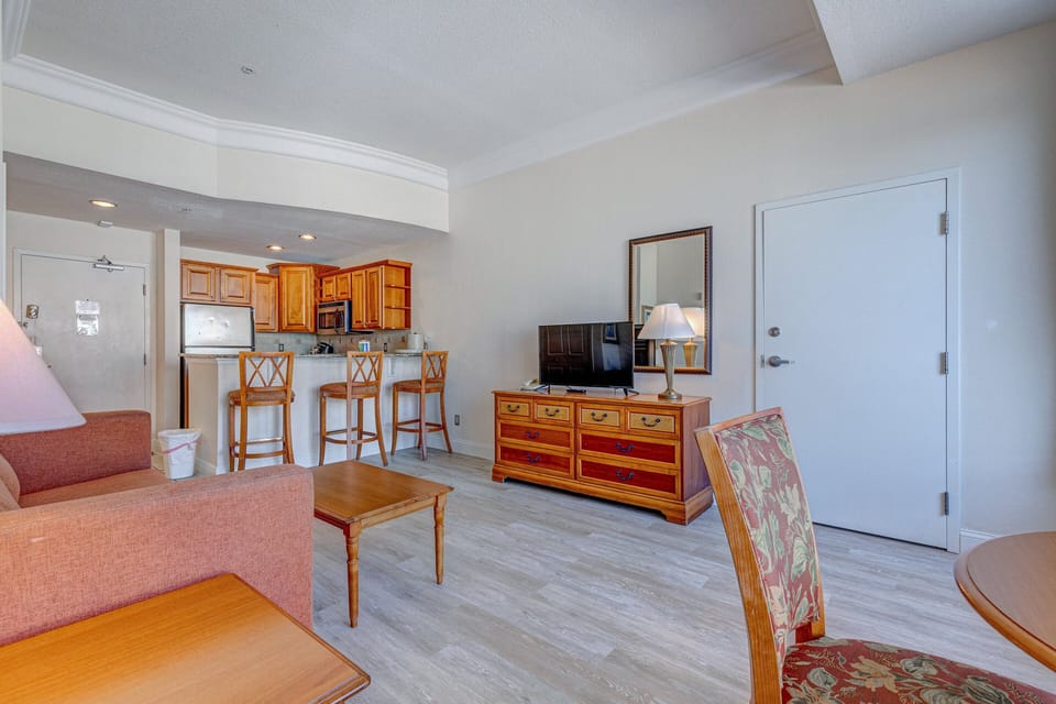 This inviting beach-stay living space offers a cozy sofa, TV, dining area, and bar seating by the kitchen—perfect for relaxing and enjoying coastal comfort throughout your stay.