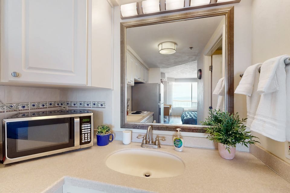 Clean, well-lit vanity area overlooking the cozy beach stay studio. Features a spacious counter, fresh linens, and easy access to the kitchen—perfect for refreshing after a day by the ocean.