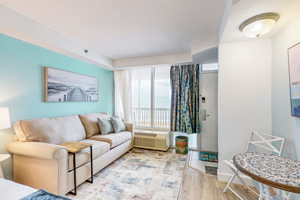 Bright and inviting living area with coastal décor, comfy seating, and stunning beach views through large windows—perfect for unwinding during your relaxing beach stay.