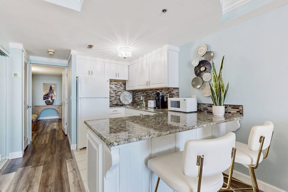 This bright kitchen features granite counters, modern bar seating, and coastal décor—an inviting space to enjoy meals and morning coffee during your relaxing beach stay.