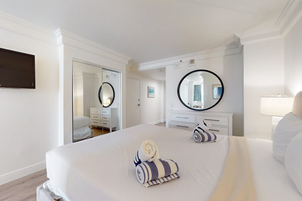 Enjoy a refreshing beach stay in this modern bedroom featuring crisp white décor, a plush bed, mirrored closet doors, and elegant coastal touches—perfect for unwinding after oceanfront adventures.