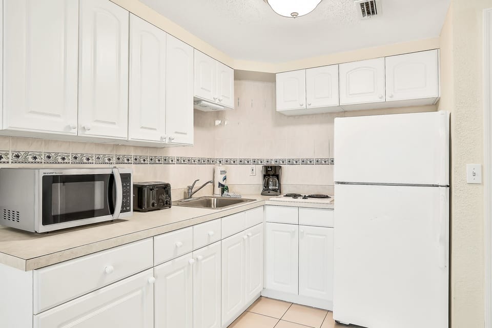 Enjoy convenient beach-stay meals in this clean, fully equipped kitchenette featuring ample cabinets, full fridge, microwave, toaster, and cooktop—perfect for simple seaside dining.