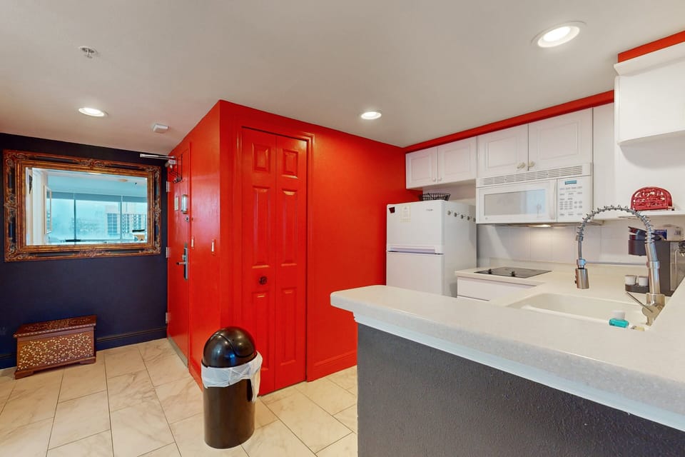 Vibrant kitchen entry with bold red accents and full amenities—perfect for easy meals during your beach stay. Ideal for relaxing after sun-soaked adventures.