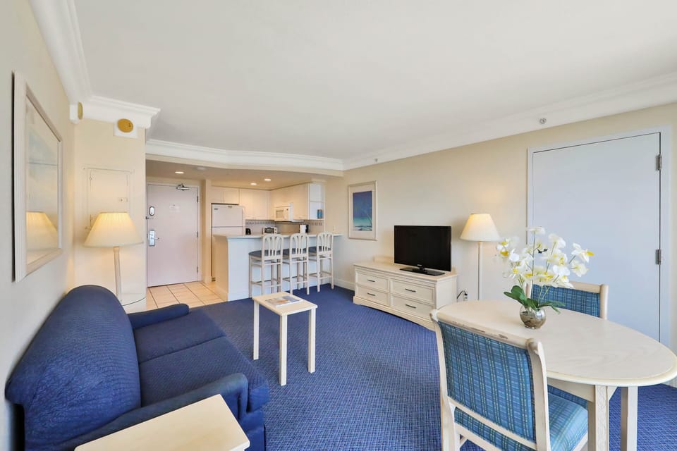 Relax in this bright beach-stay living space featuring a cozy sofa, dining area, kitchen bar seating, and coastal décor—perfect for unwinding after a day by the shore.