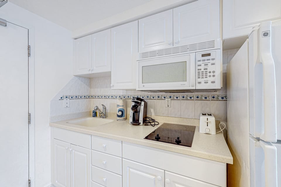Convenient in-room kitchenette with cooktop, microwave, and coffee maker—perfect for easy meals during your beach stay. Fresh white cabinetry keeps the space bright and functional.