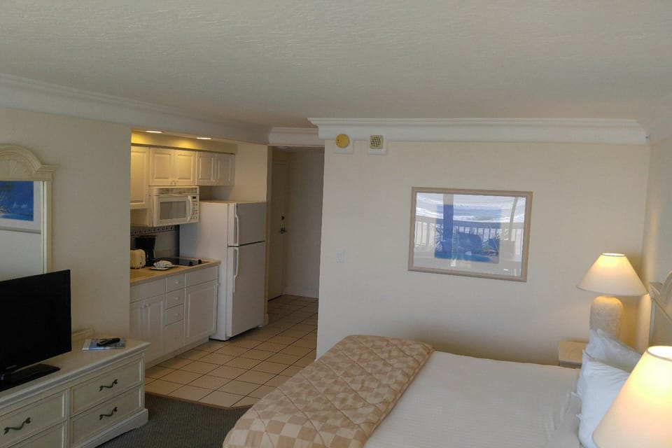 Bright beachside studio featuring a well-equipped kitchenette, comfy bedding, and warm lighting—perfect for relaxing after a sun-filled day by the shore. Ideal for a convenient and cozy beach stay.
