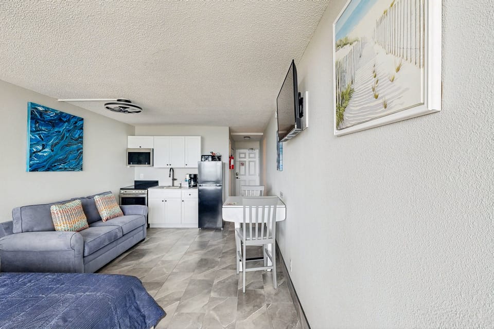 Open beachfront studio featuring a cozy bed, sleeper sofa, dining area, and full kitchenette. Perfect for a comfortable beach stay, offering coastal style and easy living just steps from the sand and ocean.