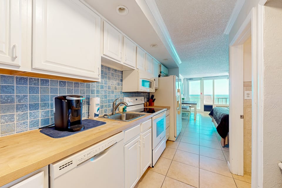 Bright coastal kitchen featuring full appliances, ample counter space, and ocean views just beyond. Ideal for a comfortable beach stay, this space makes dining in easy before heading out to enjoy the sun, sand, and sea.