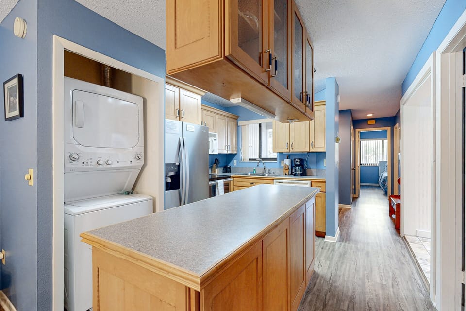 Bright, fully equipped kitchen with island counter space, stainless steel appliances, and convenient in-unit washer and dryer—perfect for extended beach stays and comfortable coastal vacation living.