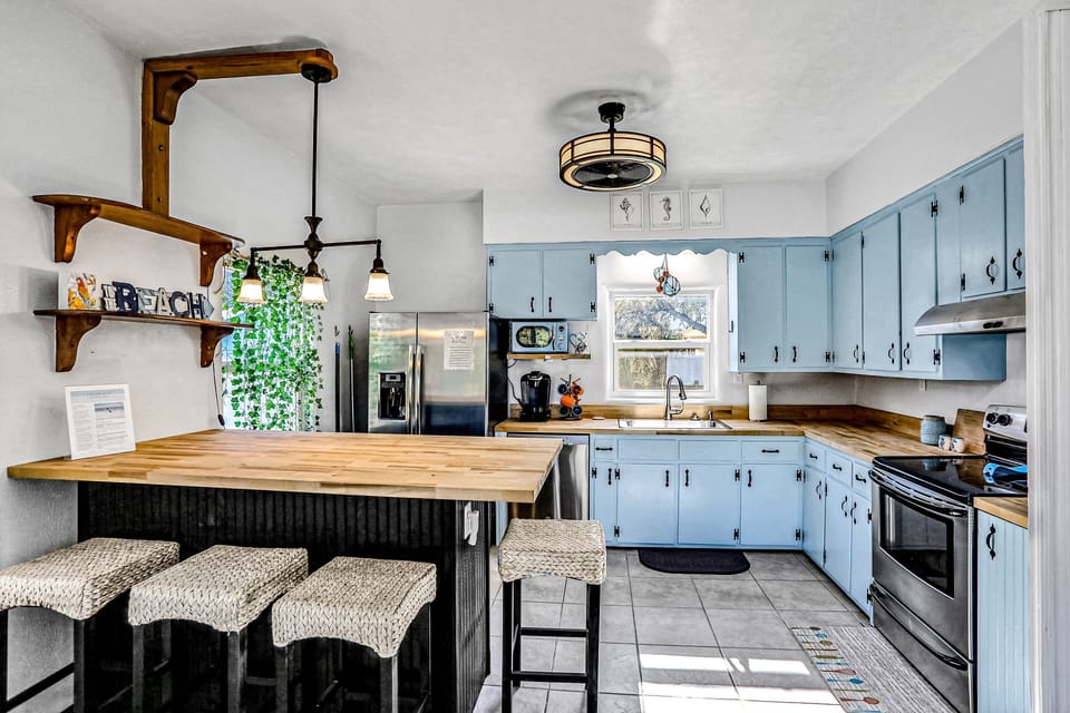 Bright beach-style kitchen with charming blue cabinets, butcher-block counters, and a roomy breakfast bar. A perfect spot to gather and enjoy meals during your relaxing beach stay.