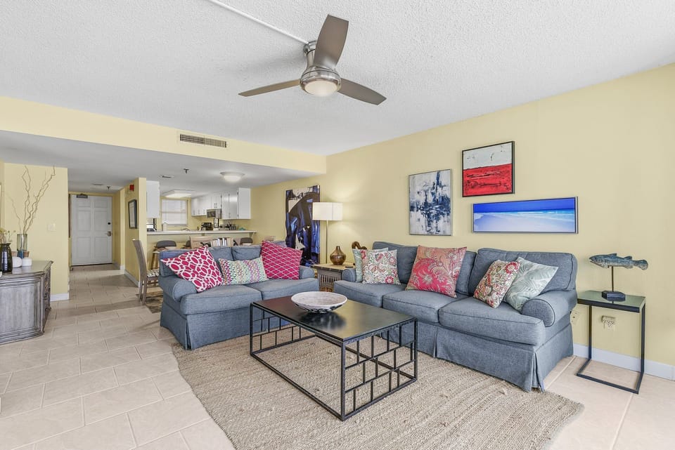Spacious living area with plush sectional seating, coastal décor, and an open layout flowing into the kitchen. Perfect for relaxing together after sunny days and creating memories during your beach stay.