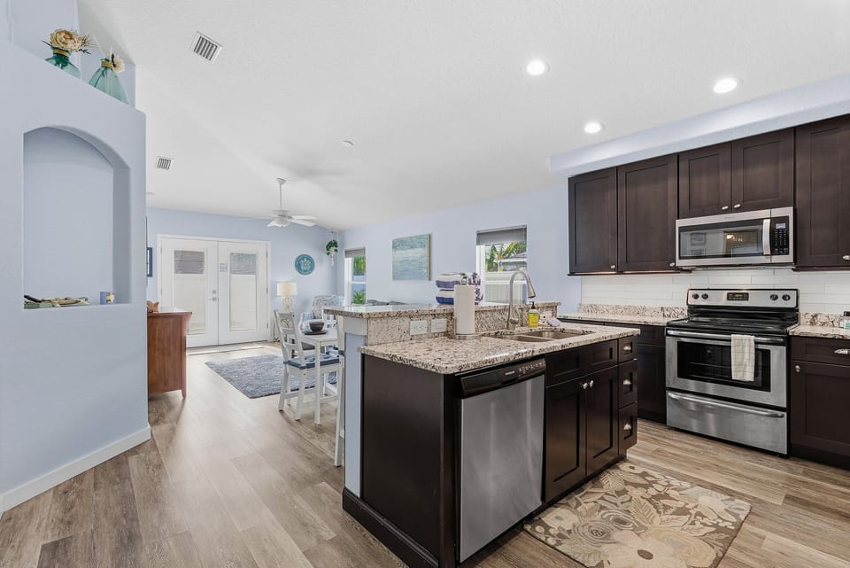 Modern open-concept kitchen with granite countertops and stainless appliances, flowing into a bright coastal living area. Ideal for cooking, gathering, and relaxing during your beach stay vacation getaway.