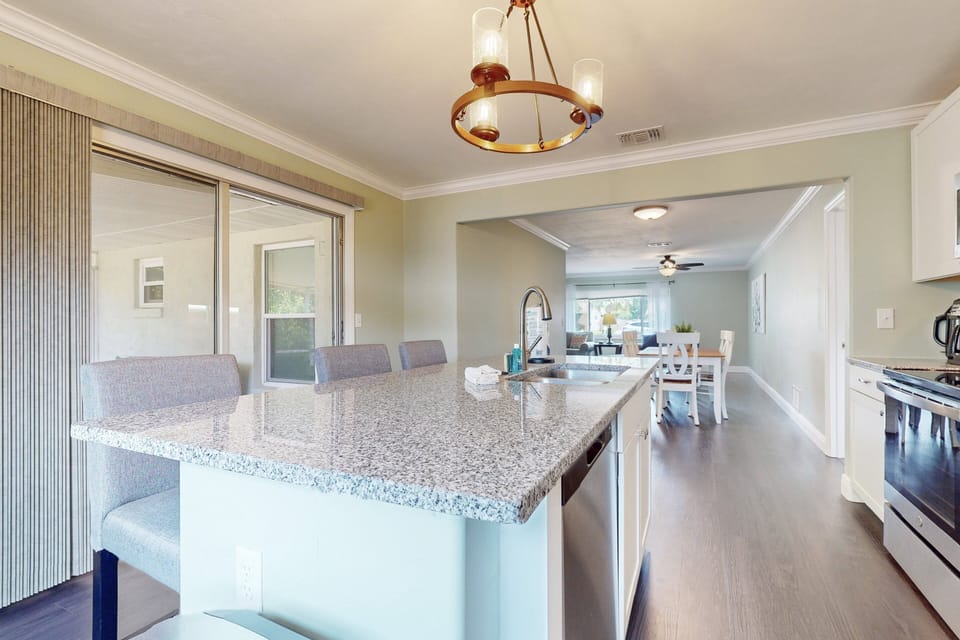 Open-concept beach-inspired kitchen and dining area with granite island seating, sleek appliances, and easy access to the patio for relaxed coastal living during your beach stay.