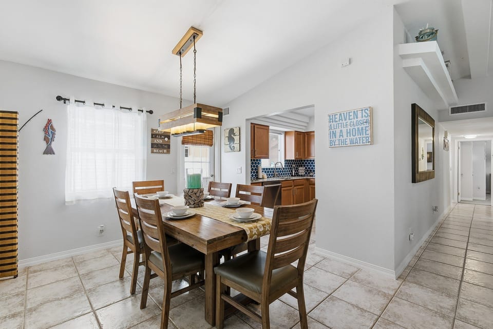 Share meals during your beach stay in this inviting coastal dining area with warm wood furnishings, beach-inspired accents, and easy access to the kitchen—perfect for family dinners and planning your next day at the beach.