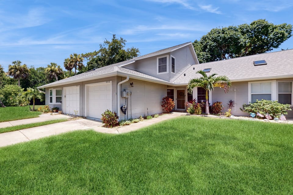 Bright, welcoming front exterior of this beachside villa featuring lush landscaping and a private garage—your perfect starting point for a relaxing beach stay.