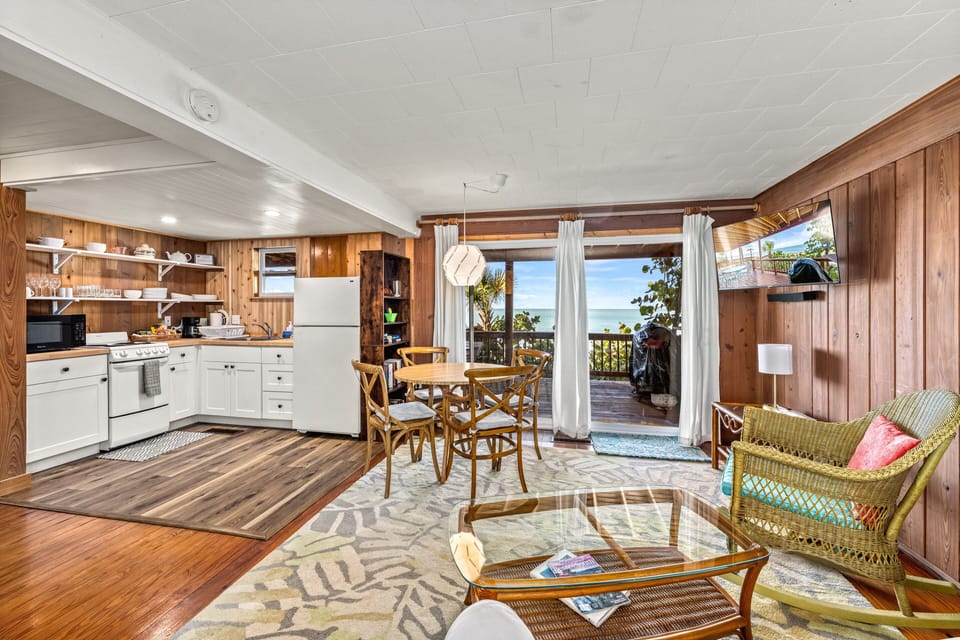 Sunlight pours through sliding doors, illuminating the open living, dining, and kitchen space with sparkling Gulf views beyond.