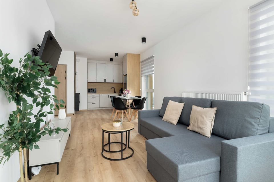 A living area with a gray sofa, coffee table, and decorative plants. Bright and welcoming ambiance.
