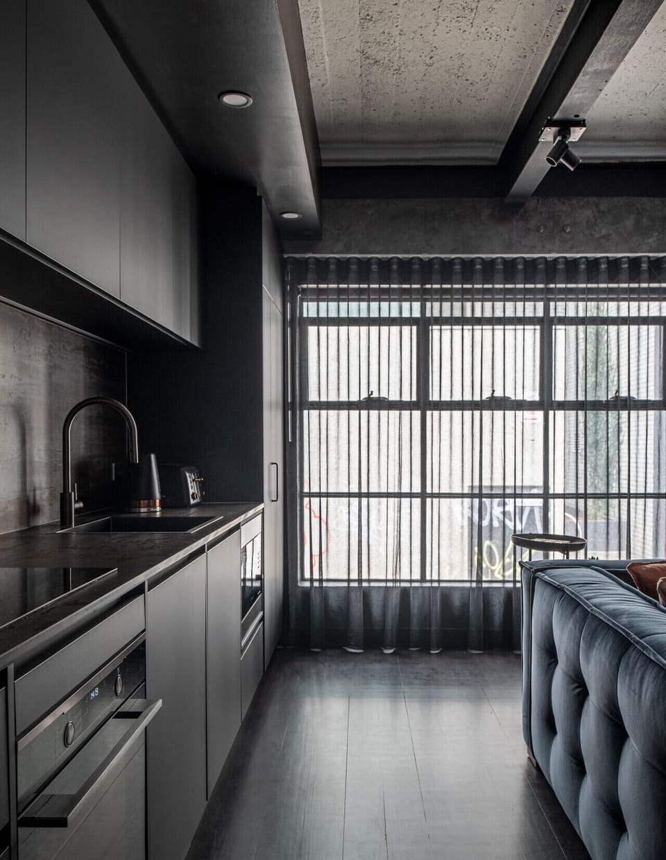 Light-filled open-plan kitchenette and living area with sleek finishes, high ceilings and sheer curtains for privacy and ambience