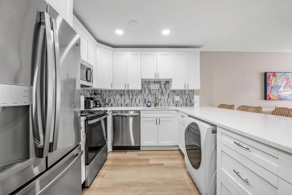 Sleek, fully stocked kitchen with stainless appliances, modern backsplash, and spacious quartz counters. Enjoy a built-in washer/dryer and ample storage—perfect for cooking, convenience, and effortless vacation living.