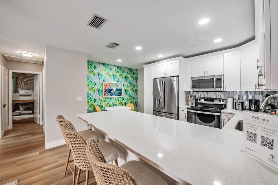 Bright, modern kitchen with sleek stainless appliances, a spacious quartz island, and stylish bar seating. Colorful wall art adds a fun, fresh vibe—perfect for cooking, gathering, and unwinding together.
