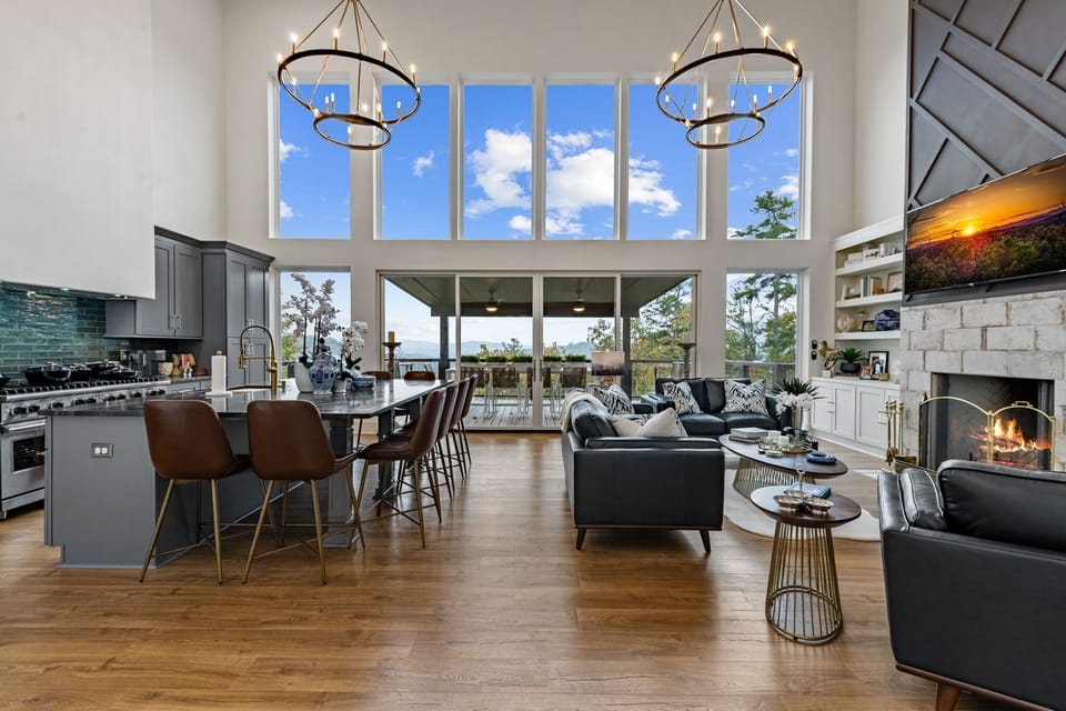 Sunlight pours through floor-to-ceiling glass, framing breathtaking mountain views from the open living room and chef's kitchen.