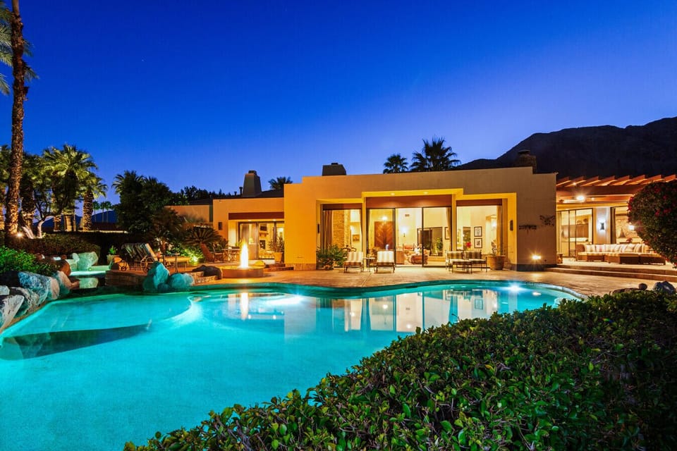 As the sun sets, the villa comes alive—glowing interiors, a shimmering pool, and mountain silhouettes create the perfect desert evening retreat.