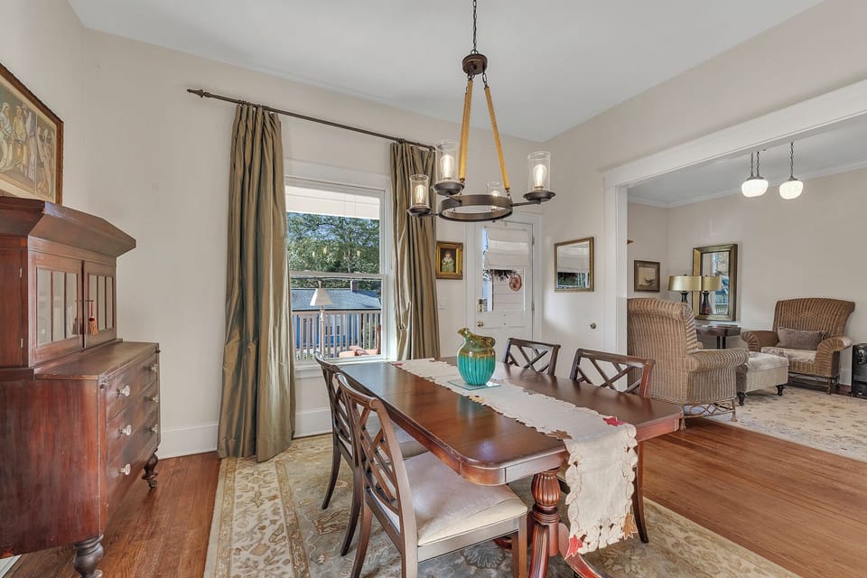 Dining area w/ wood table, chandelier & tall windows dressed in curtains