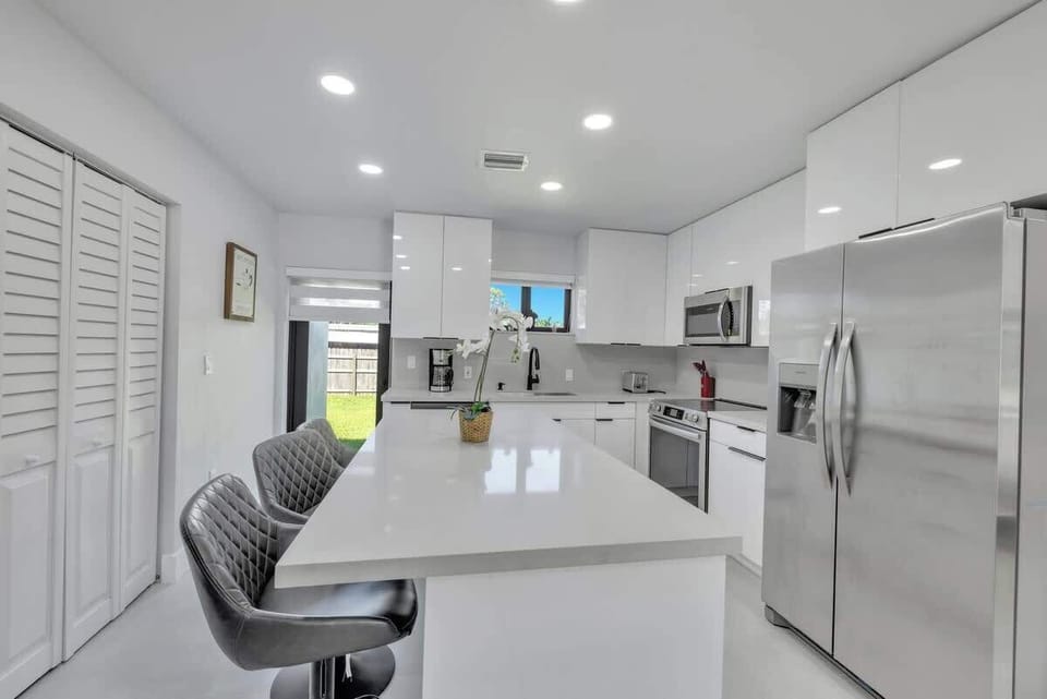 Cook and dine in style in this bright, modern kitchen featuring sleek white cabinetry, stainless steel appliances, and a spacious center island with bar seating for three. Enjoy natural light and views of the private backyard, plus a dedicated coffee