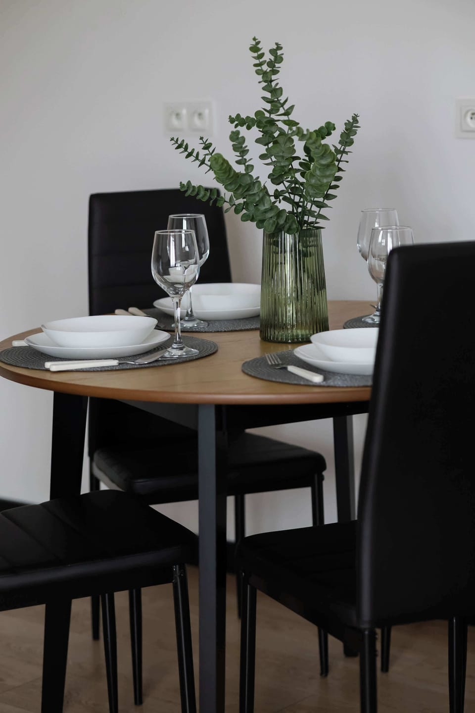 A small dining corner with a round table and two chairs placed near a wall-mounted TV. A plant adds natural color to the scene. The setup creates a practical spot for meals or work.