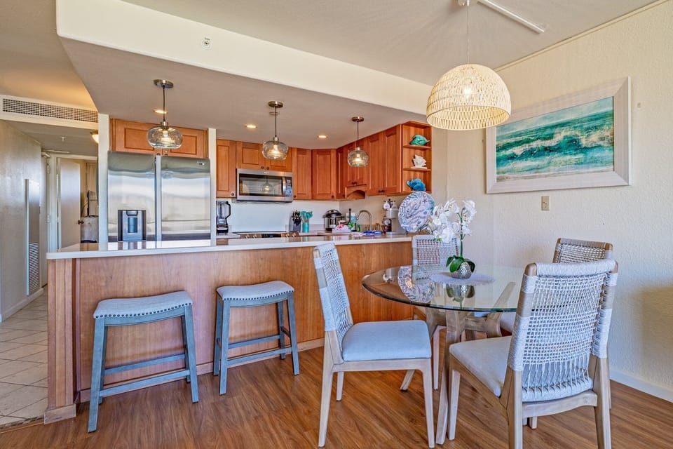Enjoy a cozy dining nook paired with a spacious kitchen, featuring a glass-top table, woven chairs, and warm wood cabinetry accented by modern stainless steel appliances.