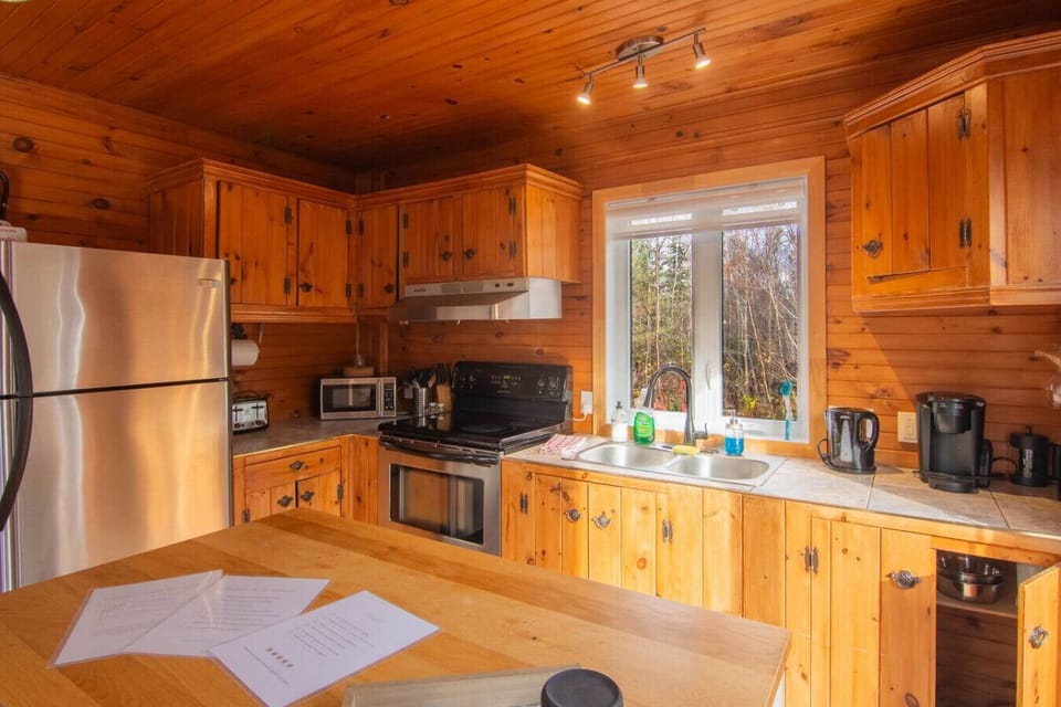 Full view of the fully equipped kitchen: oven, microwave, refrigerator, kettle and crockery provided. Warm and authentic ambiance with natural wood.
