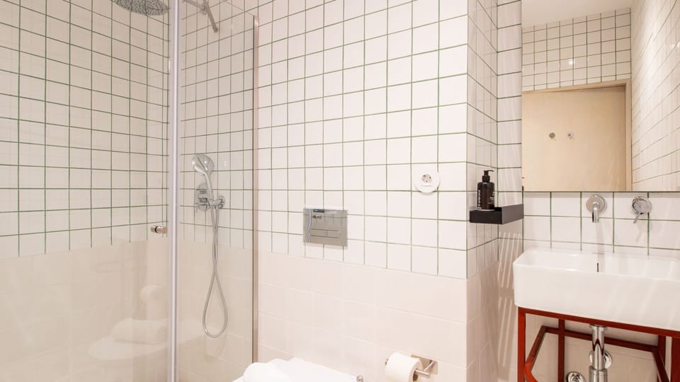 Clean lines, geometric tiles, and a striking red vanity create a bathroom that’s as functional as it is stylish. Designed to refresh, crafted to impress.#LovelyStay #ModernEssentials #MinimalLuxury #PortoLiving