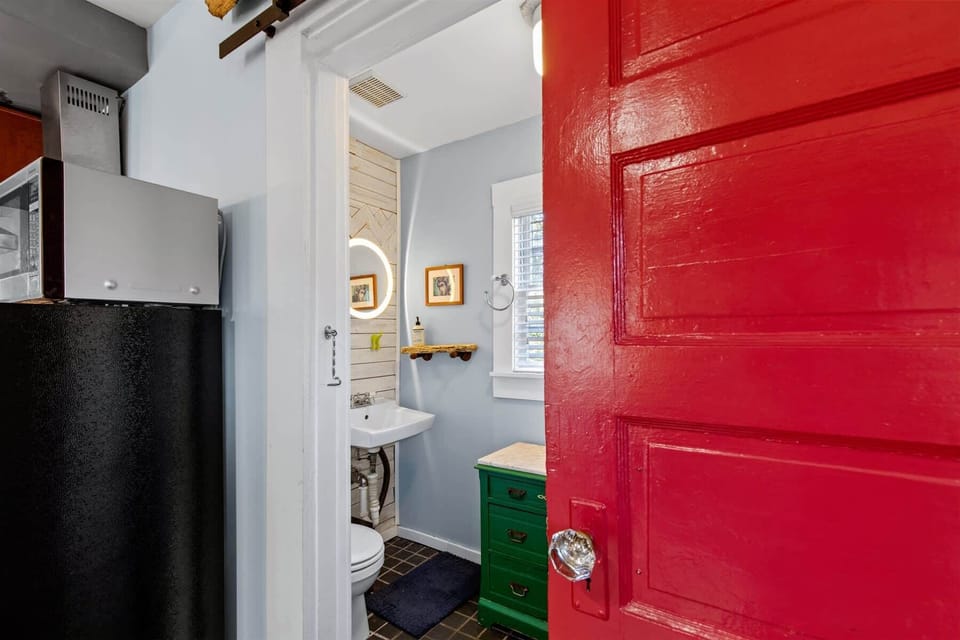 Colorful and stylish bathroom with a single vanity, mirror, and vibrant green cabinet. There are charming details throughout.