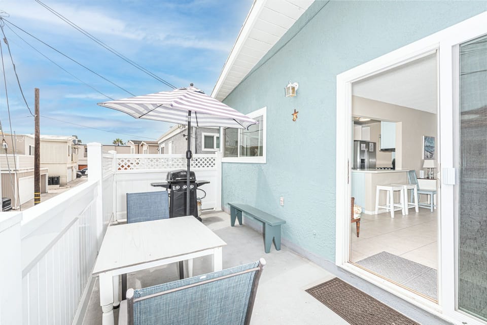 Back balcony with a small patio table for two includes additional seating bench and a propane gas BBQ grill.
                