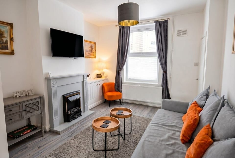 Cosy lounge with electric fireplace, large TV and plush orange accents.