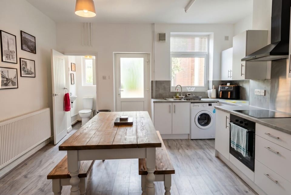 Full kitchen with oven, hob and washing machine beside a farmhouse dining table.