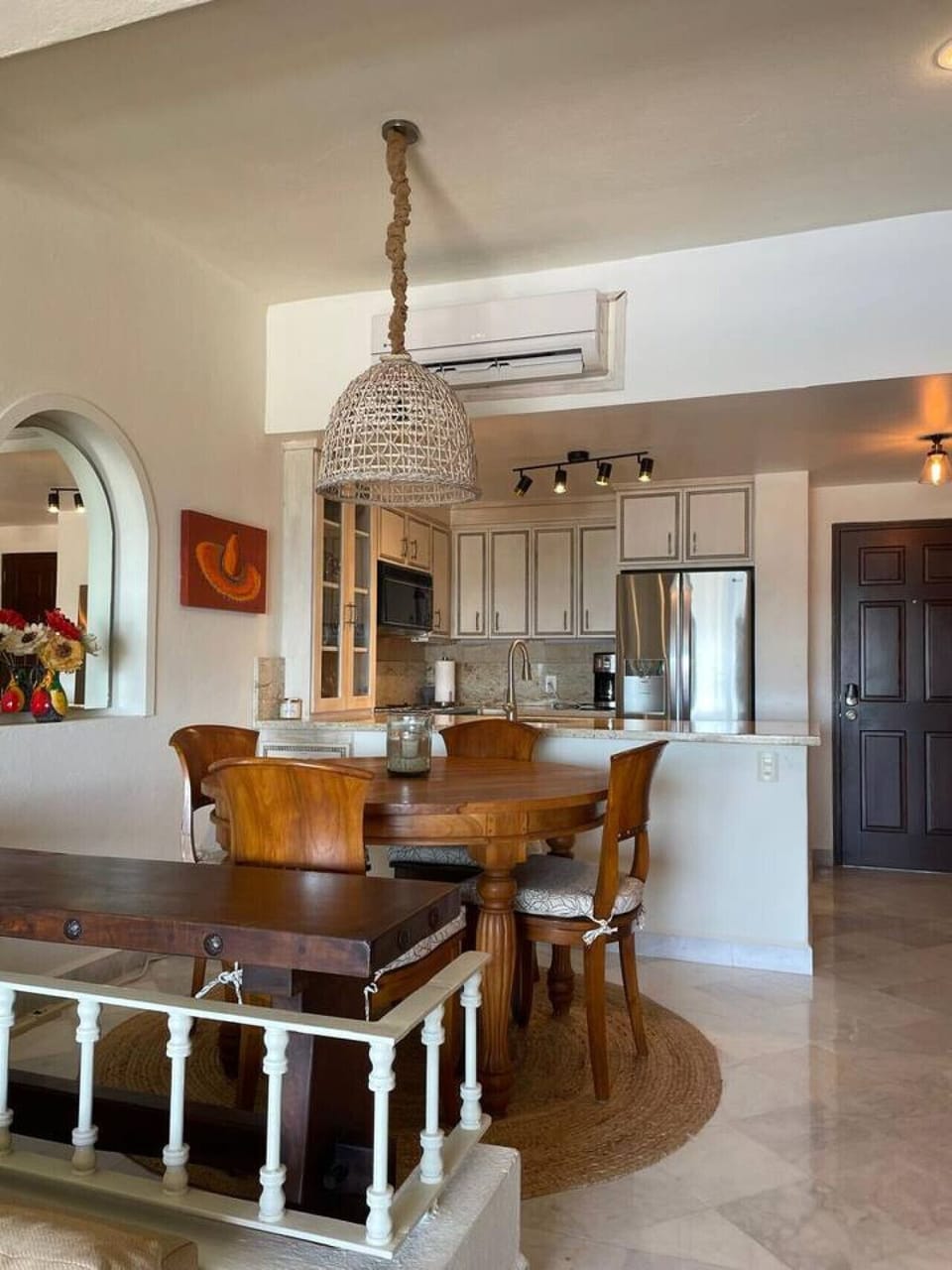 Stylish dining area with a round wooden table, woven pendant light, and easy flow to the kitchen and living room.