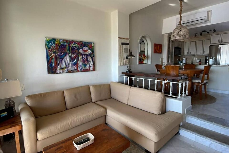 Spacious and brightly decorated living area with a comfortable sectional sofa, unique artwork, and a coffee table.
