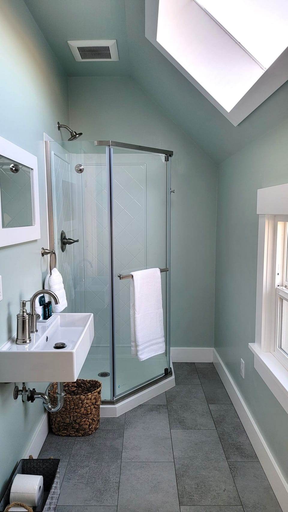 Modern bathroom with sink, shower, toilet, and storage. Skylight and window.