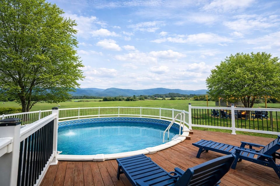Bright daytime view of the private above-ground pool with deck access from the house, lounge chairs, sunroom, and sweeping mountain vistas—your summer splash zone and relaxation retreat.